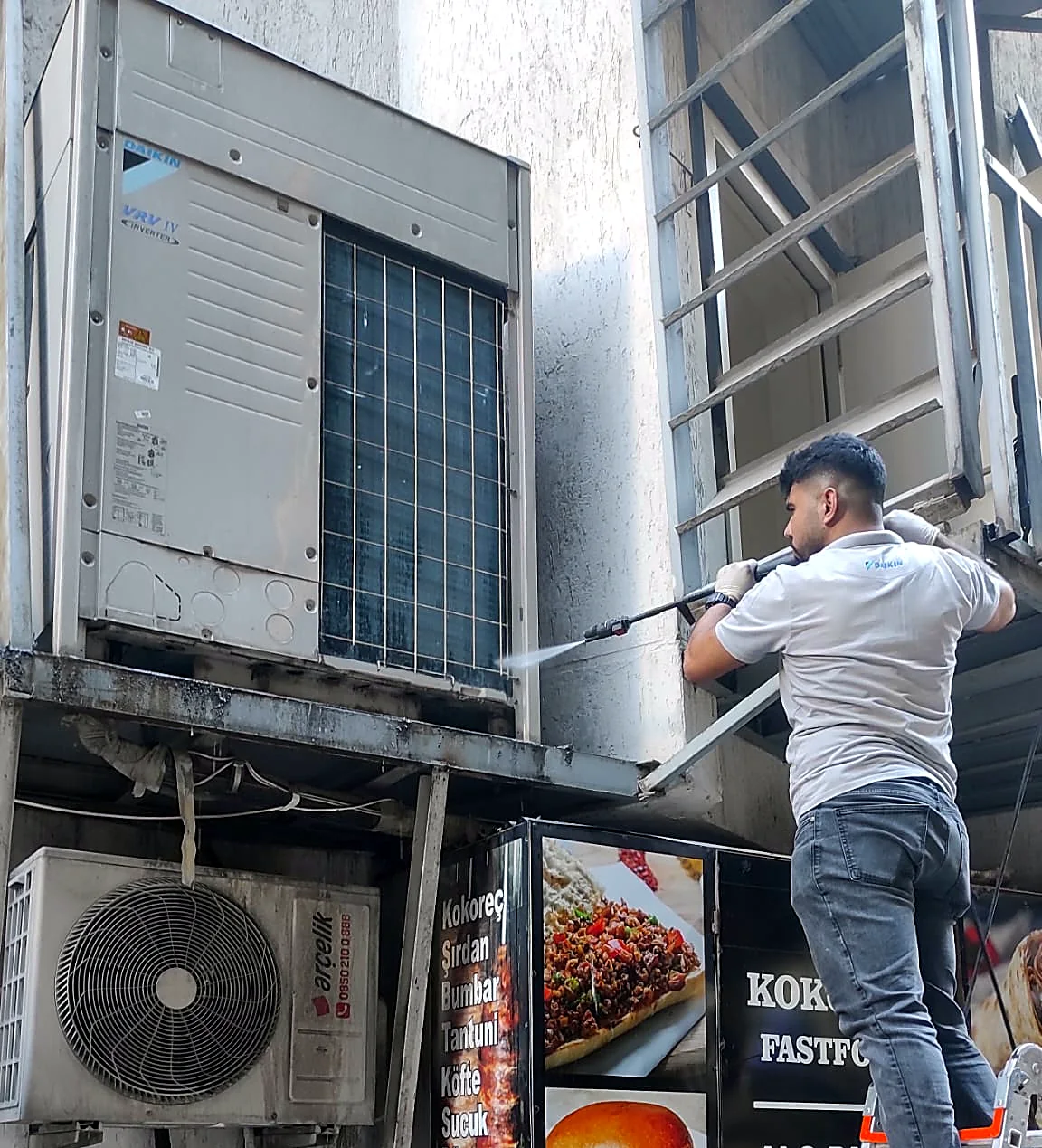 Teknisyen merdiven üstünde Daikin VRV IV dış üniteyi basınçlı suyla yıkıyor